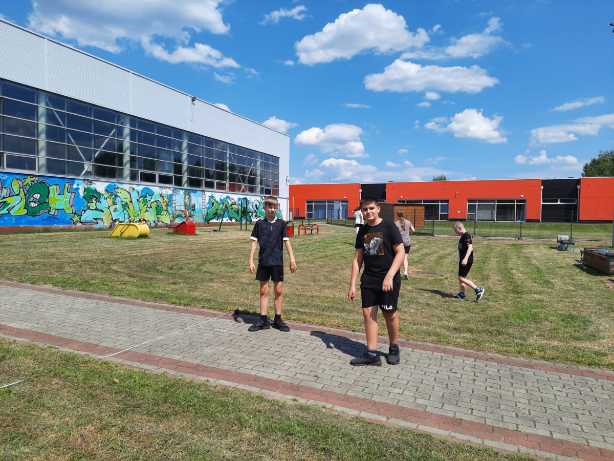 Kadr przedstawia uczniów na szkolnym boisku przed rozpoczęciem Szkolnych Mistrzostw w Lekkoatletyce 